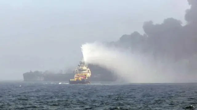 Un barco lanza agua a unos de los navíos siniestrados.