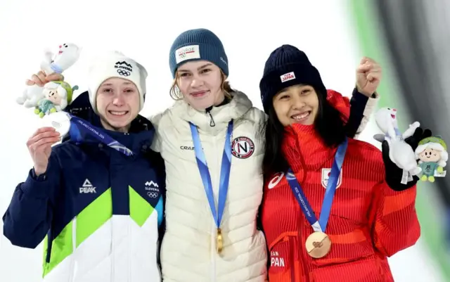 3人がメダルを首から下げて肩を組んで立っている。手には大会マスコットのぬいぐるみを持っている