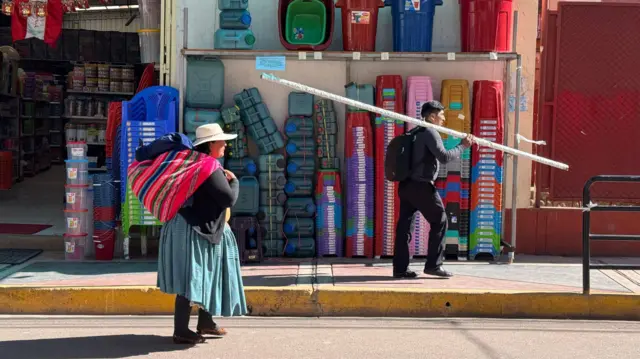Una mujer indígena y un hombre caminan frente a un comercio que vende artículos de plástico en Desaguadero, Puno, Perú.