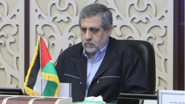 Saeed Izadi bir toplantıda İran bayrağı önünde boş bakarken görülüyor