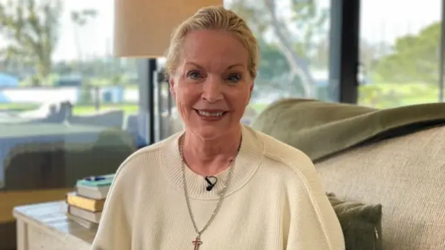 Женщина в белом свитере, поверх свитера надет крестик