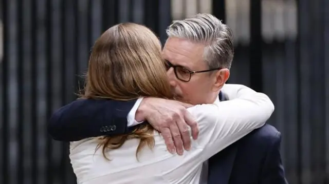 目を閉じて妻を抱きしめる首相と、夫の首に腕を回して抱きしめる白いシャツ姿のヴィクトリアさんの背中