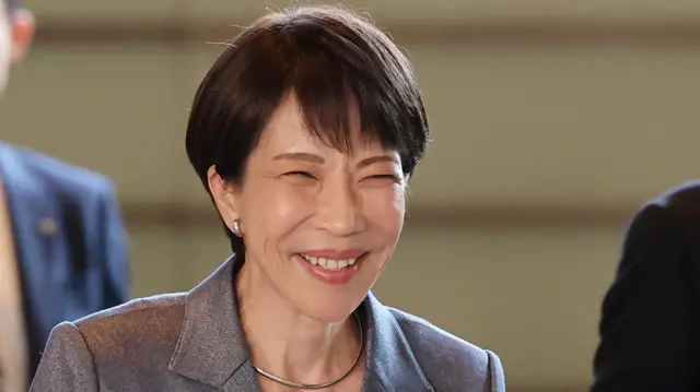 Takaichi smiles as she arrives at the prime minister's office in Tokyo, on 5 February 5 2026. She has short black hair and is wearing a silver earring and silver necklace. Her jacket is grey and she has a black blouse.