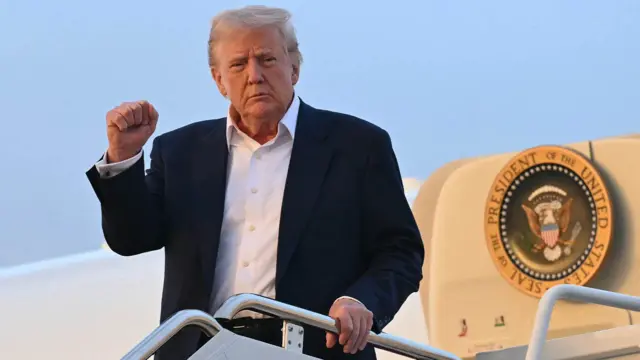 Президент США Дональд Трамп піднімає кулак в гору на трапі літака 