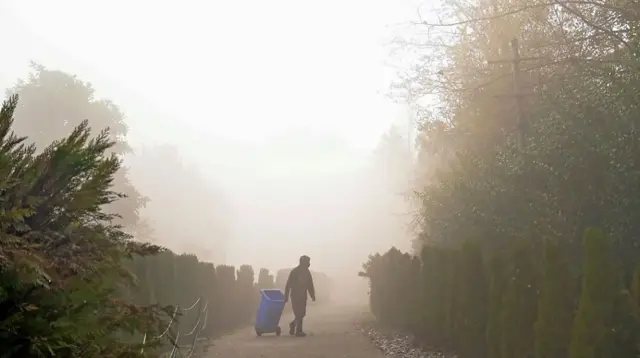 Un homme tenant un bac à ordures dans le brouillard.