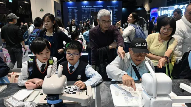 2025年12月19日：在香港会议展览中心举行的首届香港人工智慧艺术节上，老年人（右）和学生们与人工智慧机器人下棋。