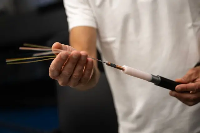 Fiber optik kabloların fotoğrafı. Bir adam elinde içinden farklı renklerde muhtelif kablolar geçen bir kabloyu kameraya gösteriyor.