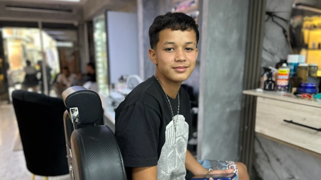 Deivi, con una camiseta negra con un diseño, mira a cámara sentado en u sillón de peluquería