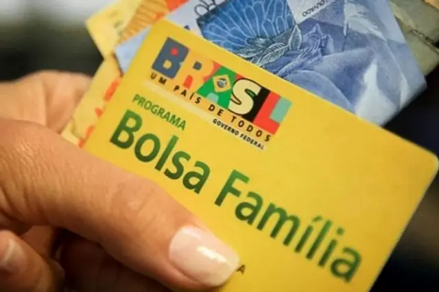 Mão feminina segurando um cartão do Bolsa Família e cédulasf12 bet jogo do foguetedinheiro