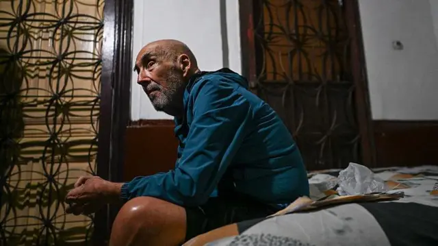 José Breijo sentado en colchón frente a su casa.