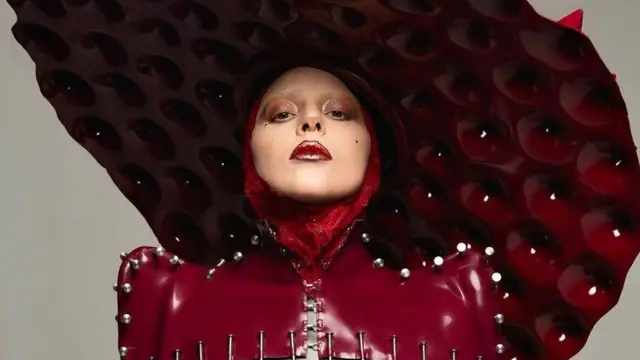 Lady Gaga usa uma roupa de vinyl vermelho-sangue, costurada com pregos e coberta por um chapéu enorme em forma de disco