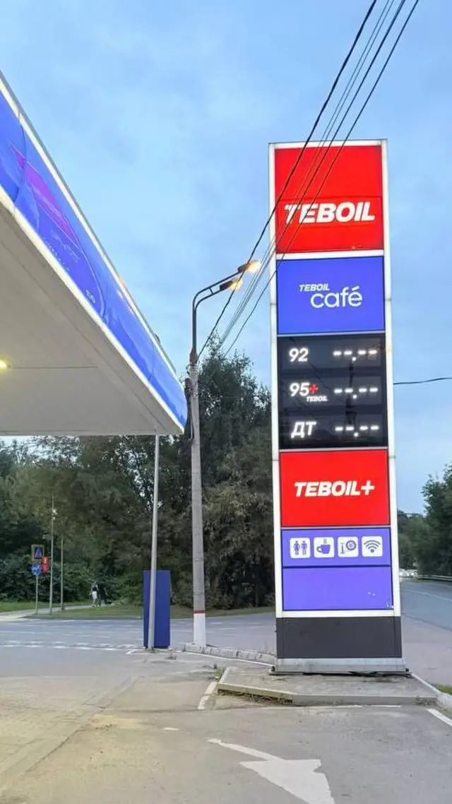На заднем плане — голубое небо. На среднем — зеленые деревья. На переднем — стойка заправки Teboil. На ней видно, что никакого топлива в продаже нет.