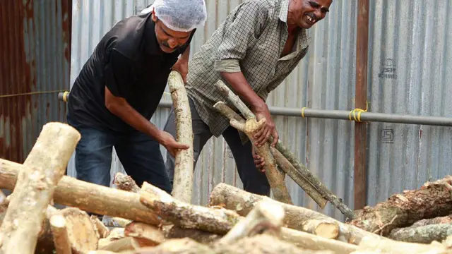 एलपीजी की कमी का रेस्तरां और होटलों पर सीधा असर पड़ा है और कई वैकल्पिक ईंधन का इस्तेमाल कर रहे हैं. तस्वीर में कोच्चि के एक रेस्तरां कर्मचारी जलाने के लिए लकड़ी ले जाते हुए