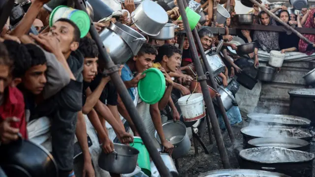 Pessoas, incluindo meninos, esperam na fila para receber refeições quentes distribuídas pela GHF na Cidade de Gaza