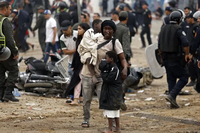 Seorang ibu mengendong anaknya di lokasi bentrokan di dekat Fnideq, perbatasan Maroko-Spanyol, pada 31 Juli 2026. Ribuan migran menyeberang dari Maroko ke wilayah Ceuta di Afrika Utara.