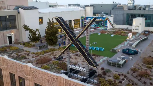 Новый логотип Х возводится на здании штаб-квартиры компании. Но фото, сделанном сверху кроме логотипа Х видны лужайка, столы и стулья, а также газоны&nbsp;— на крыше многоэтажной постройки