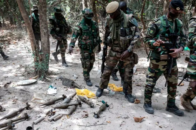 Des membres des forces armées sénégalaises passent devant des roquettes abandonnées dans une base rebelle du MFDC capturée dans la forêt de Blaze, le 9 février 2021. 