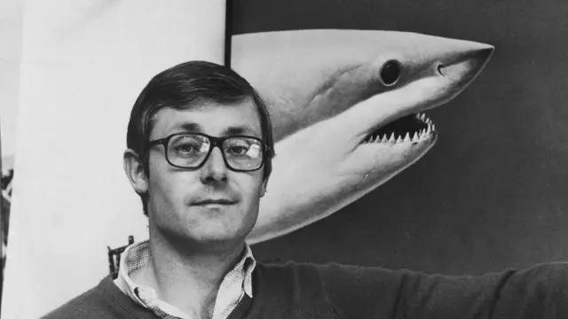 Peter Benchley siyah beyaz fotoğrafa bir köpekbalığı fotoğrafının önünde.