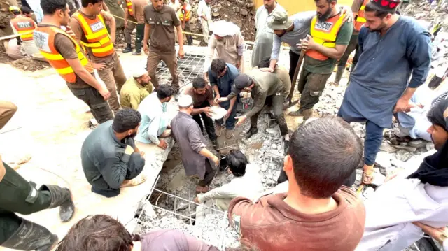 ধসে পড়া ভবনের ধ্বংসস্তূপ সরানোর চেষ্টা করছে কয়েকজন উদ্ধারকর্মী ও তাদের চেয়ে বেশি সংখ্যক সাধারণ লোকজন