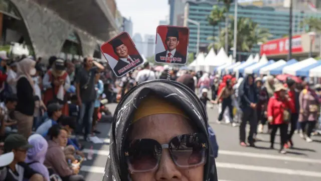 Seorang perempuan berpose dengan foto Presiden terpilih Prabowo Subianto dan wakil presiden terpilih Gibran Rakabuming Raka serta para simpatisan menunggu pelantikan mereka di Jakarta pada 20 Oktober 2024.