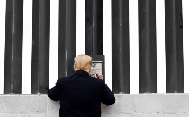 Donald Trump assinando uma placaleao betum muro