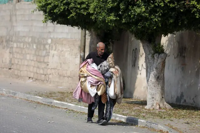 गज़ा में इसराइली हमले में तबाह घर को छोड़कर जाता फ़लस्तीनी नागरिक