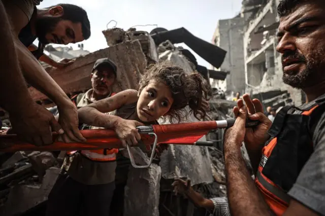 Una niña, llena de polvo, se aferra a una camilla cuando es sacada de entre los escombros por los rescatistas