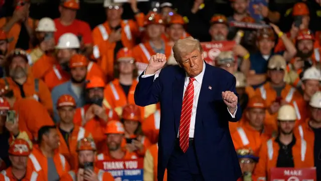 Trump gesticula frente a un grupo de obreros en una fábrica. 