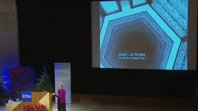 Arnold durante su discurso en Suecia con una ilustración que hace referencia a La Biblioteca de Babel en el fondo