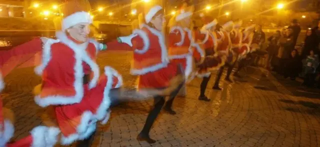 Kırmızı pelerinli Noel Baba giysileriyle dans eden bir grup insan