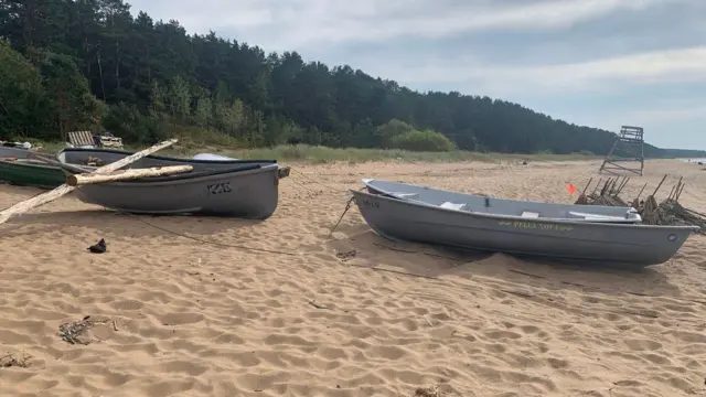 Tri čamca na peskovitoj plaži sa šumom u pozadini