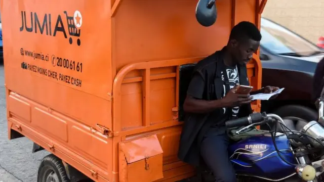 A delivery man looks at a piece of paper as he sits on a transporter with an advertisement for Nigeria's e-commerce site Jumia in Abidjan on June 13, 2019.