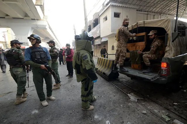 په عکس کې یو شمېر پولیس ښکاري چې وسلې ورسره دي، ځینې یې په ګاډي کې ناست دي او ځینې پر ځمکه ولاړ دي.