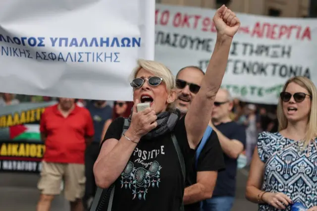 Jednodnevni štrajk radnika u Grčkoj zbog vladinog predloga da poslodavci mogu da produže radno vreme do 13 sati, žena u crnoj majici i plavom kosom drži uzdignutu pesnicu i govori u megafon