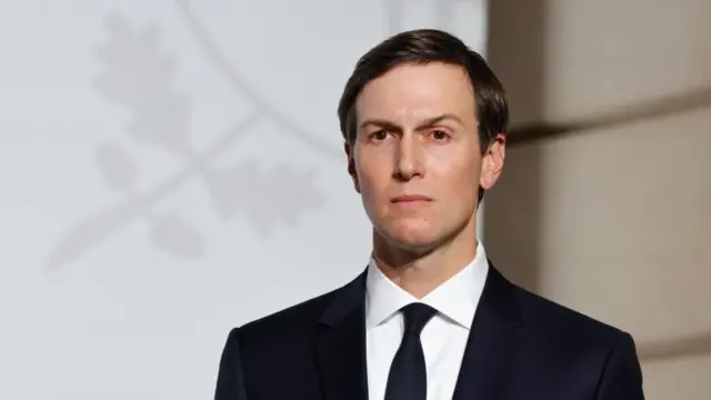 An image of Jared Kushner dressed in a black suit with a white shirt staring off into the distance. 