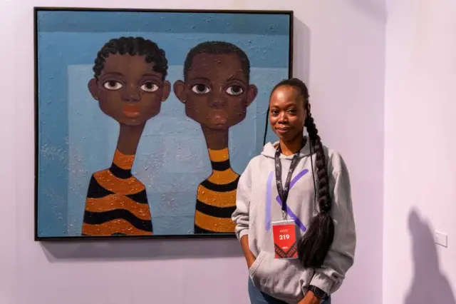 'Yar Najeriya mai zane-zane Alduphina Imuede a tsaye a kusa da wadansu zane-zane da ta yi a wajen bikin nunin zane-zane na shekara mai taken Art X da aka yi a birnin Lagos ranar Juma'a...