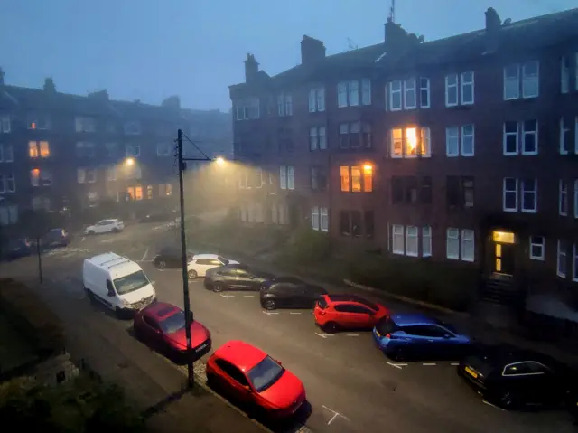 Una foto de una calle brumosa de Glasgow, con varios carros estacionados.