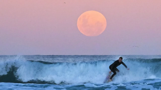 Homem surfando com Lua avermelhada atrás dele