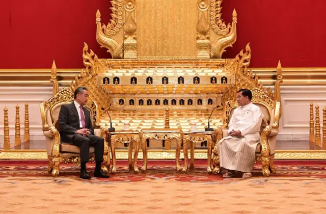တရုတ်နိုင်ငံခြားရေးဝန်ကြီးဝမ်ယိရဲ့ ၂၀၂၆ ခုနှစ်၊ ဧပြီလ ခရီးစဉ်မှာ ဦးမင်းအောင်လှိုင်နဲ့ သံတမန်ဆောင်ဧည့်ခန်းမမှာတွေ့ဆုံမှု။ နှစ်ယောက်စုလုံး ထိုင်ခုံမှာ ထိုင်နေပြီး တစ်ယောက်ဘက် တစ်ယောက် လှည့်ပြီးစကားပြောနေ။ ဝမ်ယိက အနောက်တိုင်းဝတ်စုံ ဝတ်ထားပြီး၊ ဦးမင်းအောင်လှိုင်က အဖြူရောင်တိုက်ပုံ၊ အဖြူစွက်တဲ့ပုဆိုးတို့ကို ဝတ်ဆင်ထား 