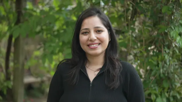 身穿黑色連身裙的普莉雅，她有一頭棕色的頭髮。