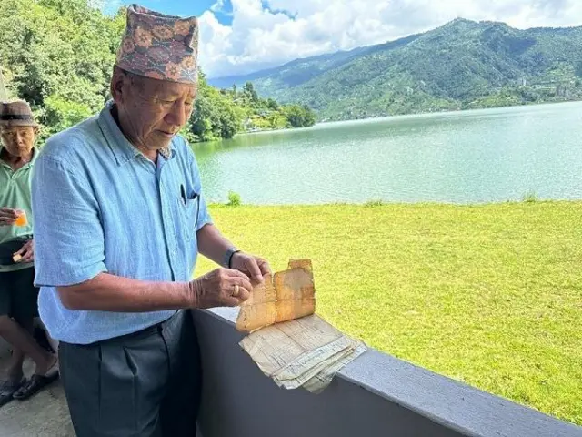 फेवातालको छेउमा उभिएर लालपुर्जा देखाउँदै देउबहादुर गुरुङ