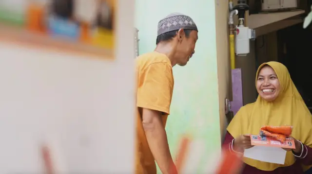 Juli membagikan kaos dan stiker kampanye ke warga di sekitar rumahnya. 