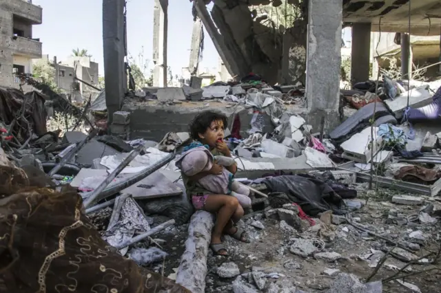 طفل يحمل دمية بين أنقاض منزل في مخيم جباليا للاجئين في قطاع غزة، في 11 سبتمبر/أيلول 2024