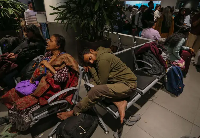 हवाई अड्डे पर बैठे, सोते परेशान यात्री