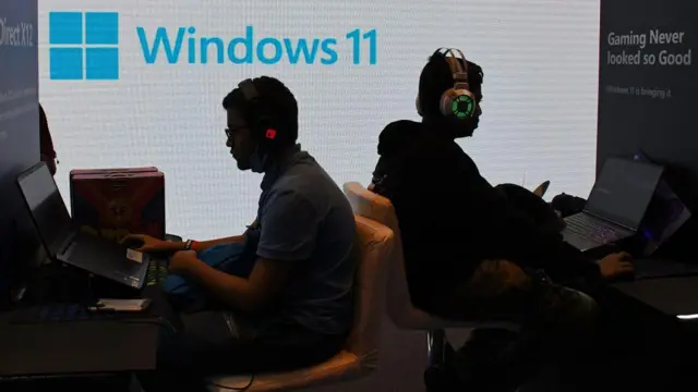 कम्प्युटर वापरत असलेले लोक, ज्यांच्या मागे विंडोजचा लोगो आहे 