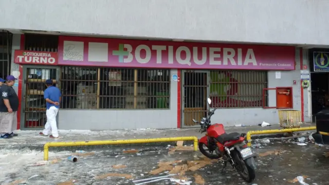 Unos hombres intentan comprar medicamentos a través de la reja de la puerta de una farmacia en Barinas.