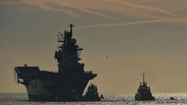 İngiliz Kraliyet Donanması'na ait hafif uçak gemisi HMS Illustrious ve ona eşlik eden bir tekne.