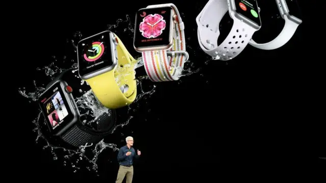 Apple CEO'su Tim Cook, 12 Eylül 2018'de Kaliforniya, Cupertino'daki Apple Park kampüsünde bulunan Steve Jobs Tiyatrosu'nda düzenlenen özel bir Apple etkinliğinde konuşma yaparken, siyah gömlek ve bej pantolon giymiş halde, Apple Watch modellerinin büyük bir fotoğrafının yer aldığı bir arka plan önünde, ellerini göğsünün önünde kaldırmış bir şekilde sahnede duruyor.