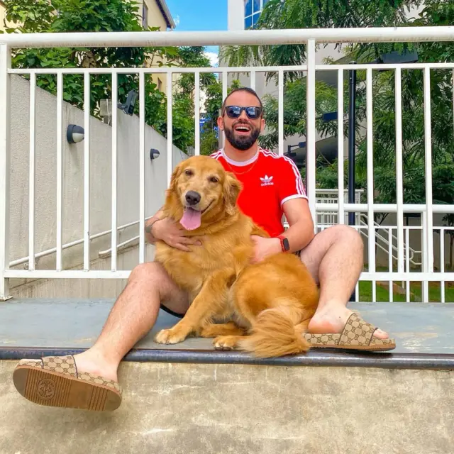 Darley, usando óculos escuros e camiseta vermelha, sorri enquanto abraça Clark, seu cão-guia