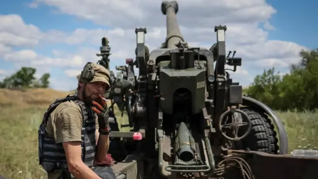 A Ukrainian service member smokes near a towed howitzer FH-70 at a front line,